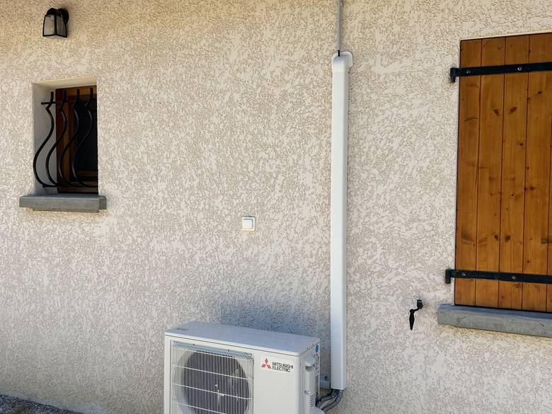 Unité extérieure de climatisation réversible Mitsubishi Electric posée en façade avec goulotte alignée, en Drôme
